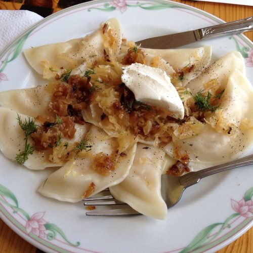 A plate of dumplings topped with sautéed onions, sauerkraut, and a dollop of sour cream, garnished with herbs.