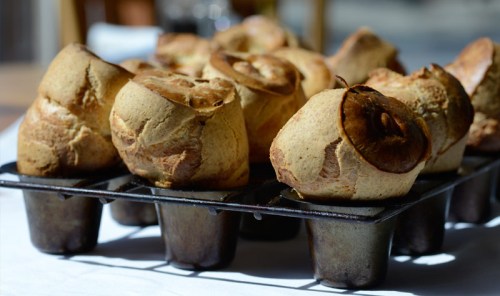A tray of golden-brown Yorkshire puddings, freshly baked and rising, on a white tablecloth.