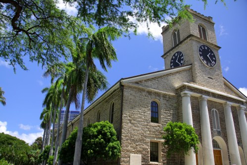 Historic stone church with a clock tower, surrounded by palm trees and blue skies.