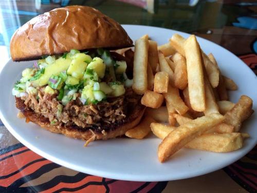 A pulled pork sandwich topped with pineapple salsa, served with a side of golden French fries on a white plate.