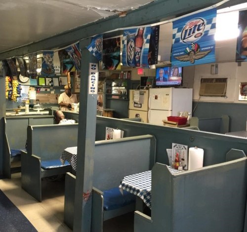 Interior of a casual diner with blue booths, checkered tablecloths, and beer advertisements on the walls.
