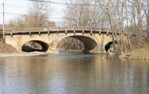 A stone bridge with arches spans a calm river, surrounded by bare trees and a clear sky.