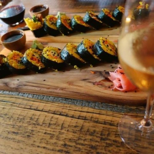 A wooden platter with colorful sushi rolls, accompanied by dipping sauces and a glass of wine.