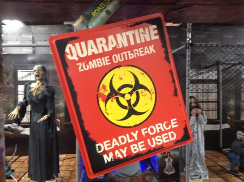 A sign reading "Quarantine Zombie Outbreak" with a biohazard symbol, warning of potential deadly force.