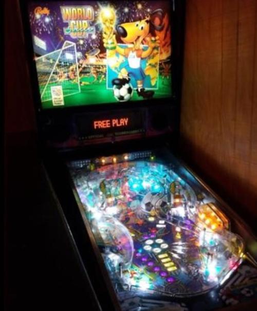 A brightly lit pinball machine featuring a soccer theme, titled "World Cup," with colorful lights and a cartoon mascot.