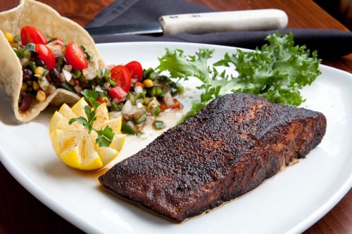 Grilled fish fillet with lemon, served alongside a fresh salad and a tortilla filled with vegetables and tomatoes.