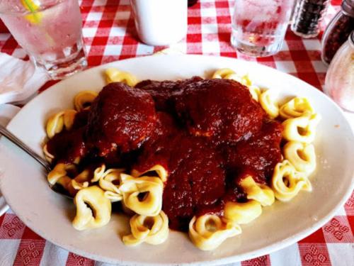 A plate of tortellini topped with meatballs and marinara sauce, served on a checkered tablecloth.