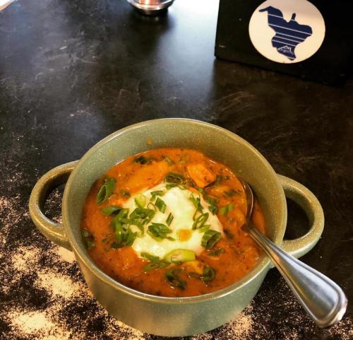 A bowl of creamy chicken curry topped with green onions, served with a spoon on a dark table.
