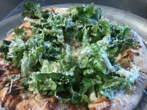 A pizza topped with fresh greens and grated cheese on a golden crust.