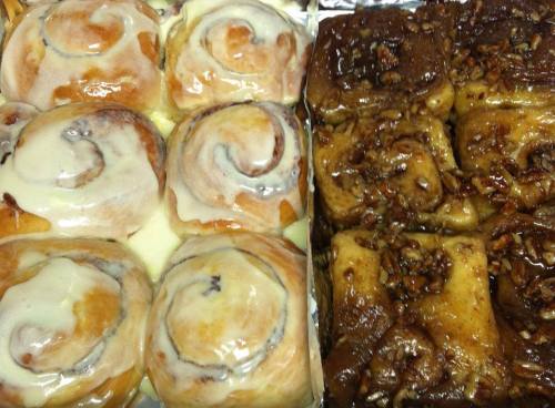 A tray of cinnamon rolls with cream cheese icing beside sticky pecan rolls, both freshly baked and golden brown.