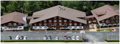 Aerial view of a large, brown, multi-story building with balconies, surrounded by trees and a parking lot.