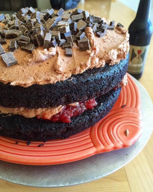 A layered chocolate cake topped with chocolate shavings and filled with cherry filling, on an orange plate.
