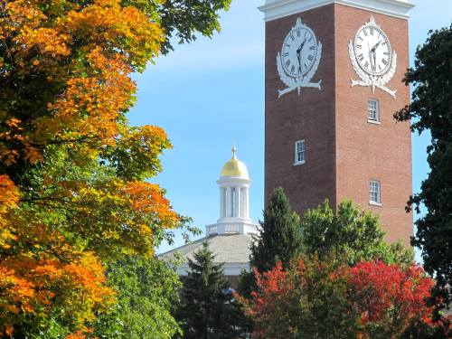 A clock tower with a golden dome surrounded by vibrant autumn foliage and a clear blue sky.