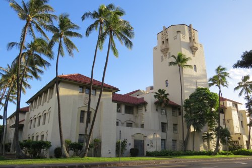 Historic building with a tower, surrounded by palm trees and a clear blue sky.