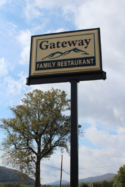 Sign for "Gateway Family Restaurant" with mountains in the background and a tree nearby under a cloudy sky.