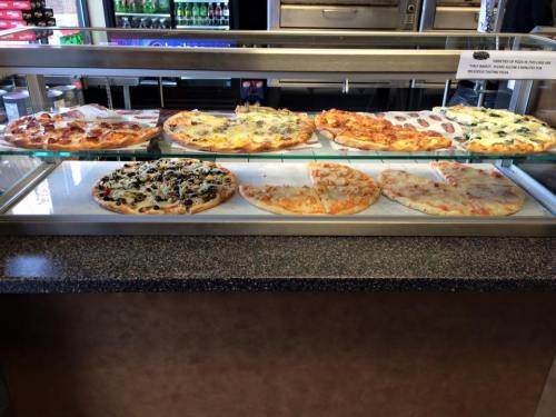 A display case with various types of pizza, including cheese, veggie, and pepperoni, in a food service area.