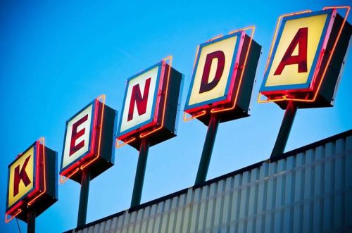 Neon sign spelling "KENDA" against a clear blue sky.