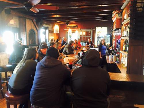 A busy bar scene with patrons seated at the counter, a bartender serving drinks, and warm, inviting decor.