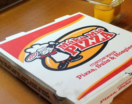 A pizza box from Maka Mia Pizza, featuring a chef graphic and text about custom-made pizza, subs, and hoagies.