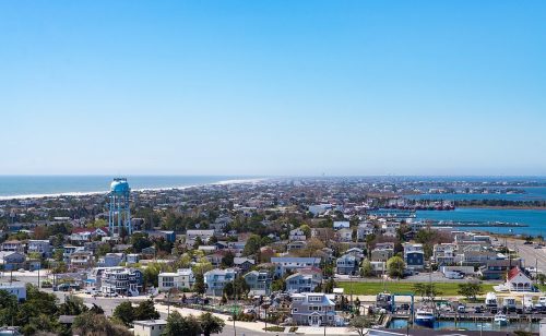 A coastal town view featuring a water tower, homes, and a clear blue sky over the ocean and harbor.