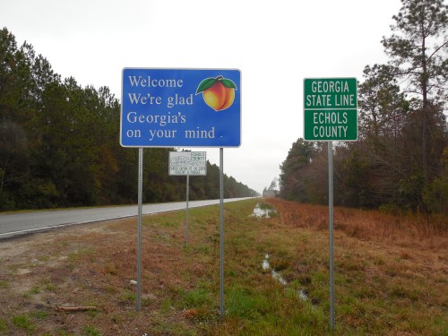 Welcome sign for Georgia with a peach graphic, alongside a sign marking the state line and Echols County.