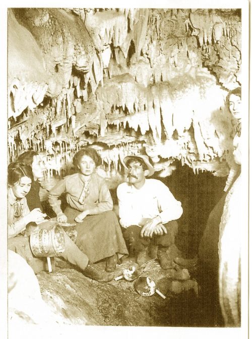 A vintage photo of four people in a cave, surrounded by stalactites and stalagmites, engaged in various activities.