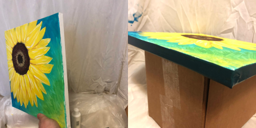 A vibrant sunflower painting on a canvas, displayed at an angle next to a cardboard box.