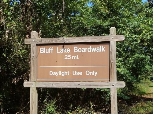 Sign for Bluff Lake Boardwalk, indicating a distance of 0.25 miles and daylight use only, surrounded by greenery.