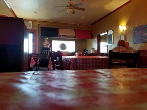 Cozy restaurant interior with checkered tablecloths, a fan, and a couple dining at a table by the window.