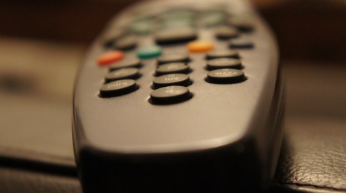 Close-up of a remote control with various buttons in focus, resting on a dark surface.