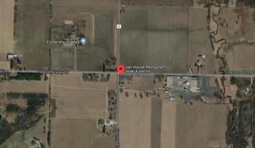 Aerial view of a rural area featuring Jalil House Restaurant, surrounded by fields and a few nearby buildings.