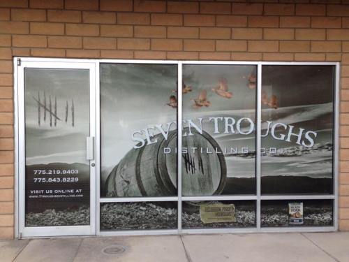 Storefront of Seven Troughs Distilling Co. featuring a barrel and birds, with a rustic design and contact information.