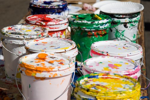 A collection of paint buckets in various colors, some with splattered paint on the lids, arranged on a table.