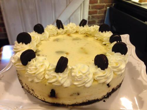A creamy cheesecake topped with whipped cream and Oreo cookies, displayed on a decorative plate.