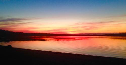 A serene lake at sunset, with vibrant orange and pink hues reflecting on the water's surface.