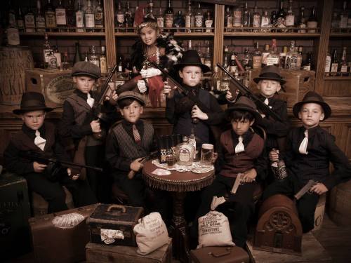 A group of children dressed in vintage gangster attire, posing with toy guns in a speakeasy setting.