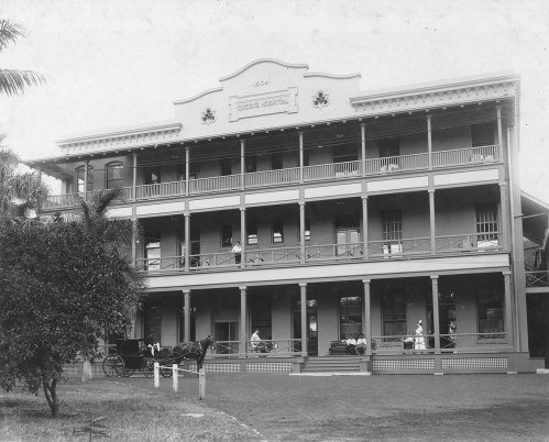 Historic black-and-white photo of a large colonial building with a horse-drawn carriage in front and people on the porch.