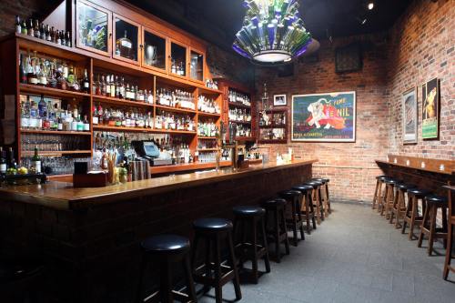 A cozy bar with a wooden counter, shelves of liquor, and vintage posters on exposed brick walls.