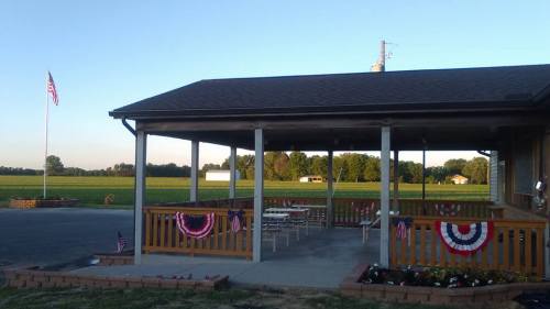A pavilion with American flags and bunting, surrounded by green fields under a clear sky.