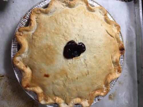 A freshly baked pie with a golden crust and a small dollop of berry filling in the center.