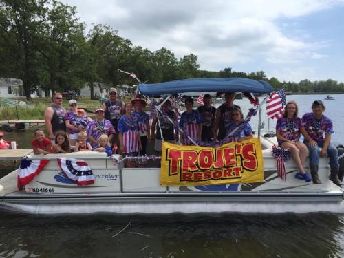 A group of people in patriotic attire on a decorated boat, celebrating by a lake with trees in the background.