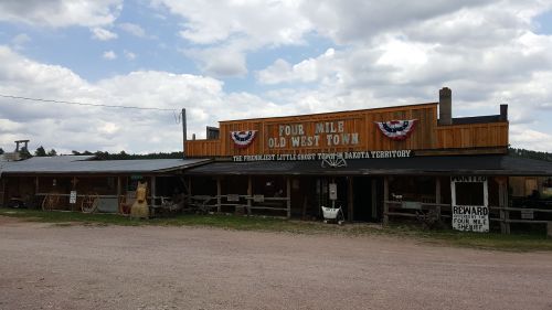 Old West-style building with wooden facade, "Four Mile Old West Town" sign, and decorative bunting under a cloudy sky.