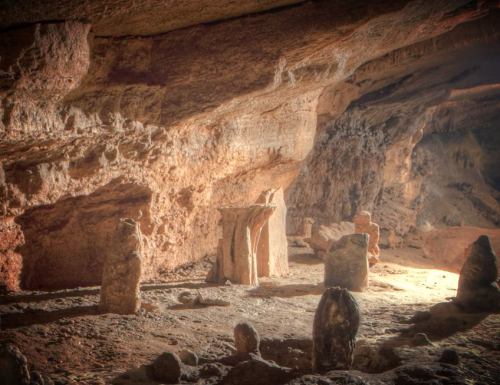 A dimly lit cave interior featuring large stone formations and a rocky floor, creating an ancient, mysterious atmosphere.