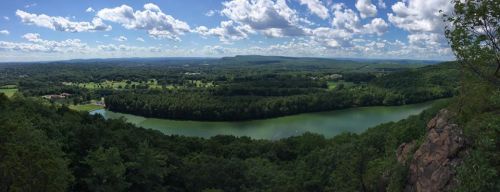 A panoramic view of a lush green valley with a winding river, under a bright blue sky with fluffy clouds.