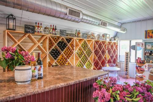 A cozy wine shop interior with wooden racks filled with bottles, a stone counter, and fresh flowers on display.