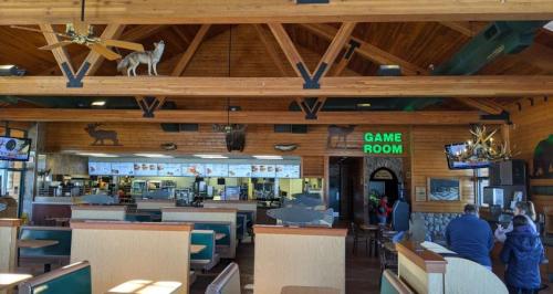 Interior of a rustic restaurant with wooden beams, game room sign, and animal decor. Customers are seated at booths.