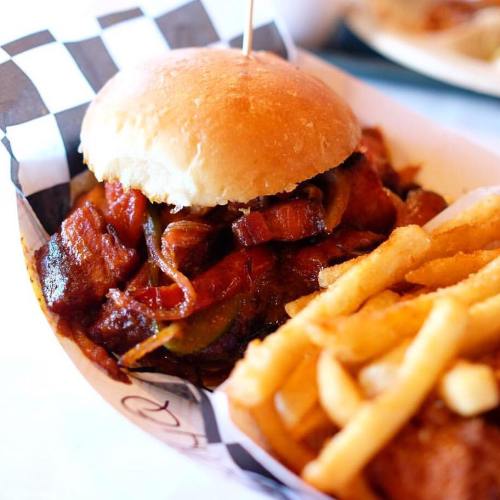 A close-up of a sandwich with grilled meat and onions, served with a side of crispy French fries.