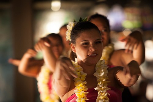 A group of dancers in floral leis perform a traditional dance, showcasing graceful movements and vibrant attire.