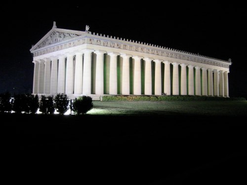 A large, illuminated classical temple with tall columns, set against a dark night sky.