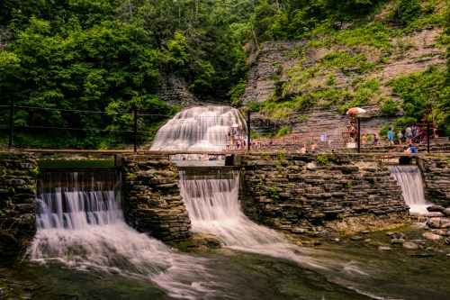 A scenic waterfall cascading over stone structures, surrounded by lush greenery and visitors enjoying the view.